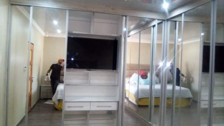 Mirrored sliding door wardrobe with a central built-in TV unit and white storage shelving.