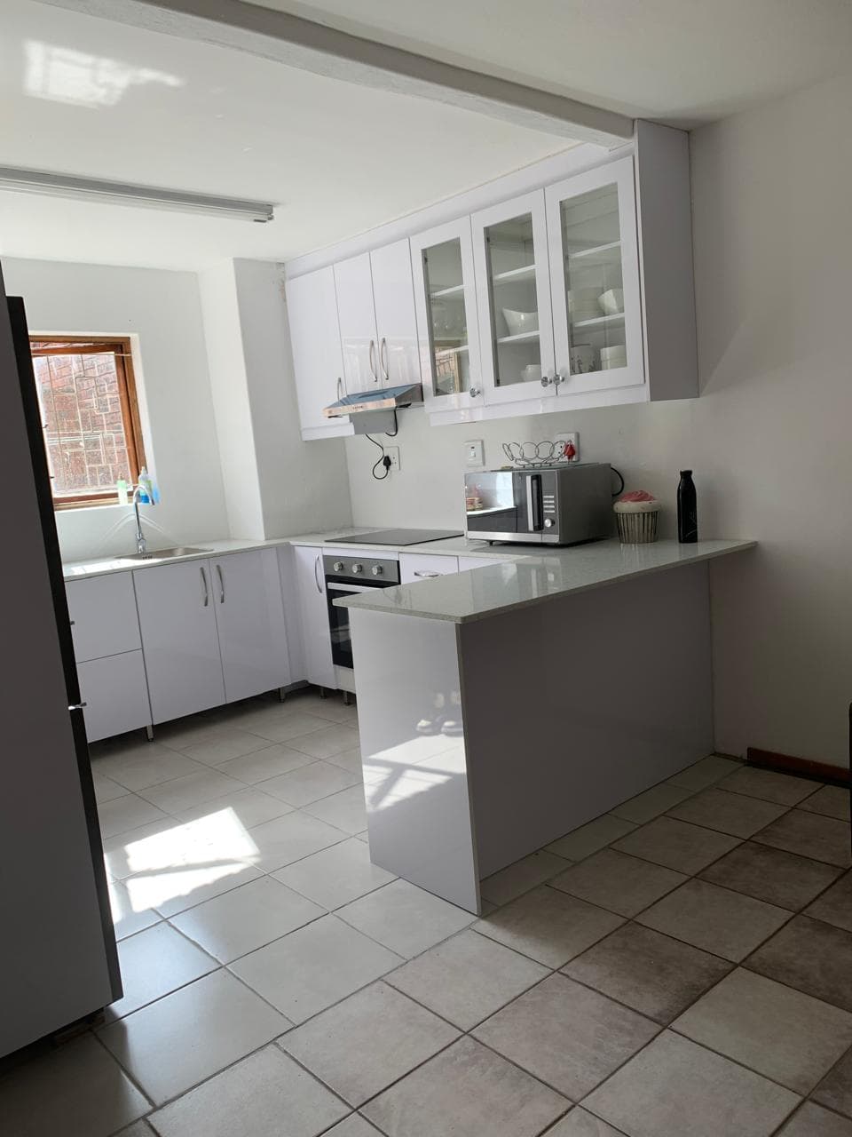 Modern white kitchen featuring minimalist cabinetry, a breakfast bar, and light grey tiled flooring.