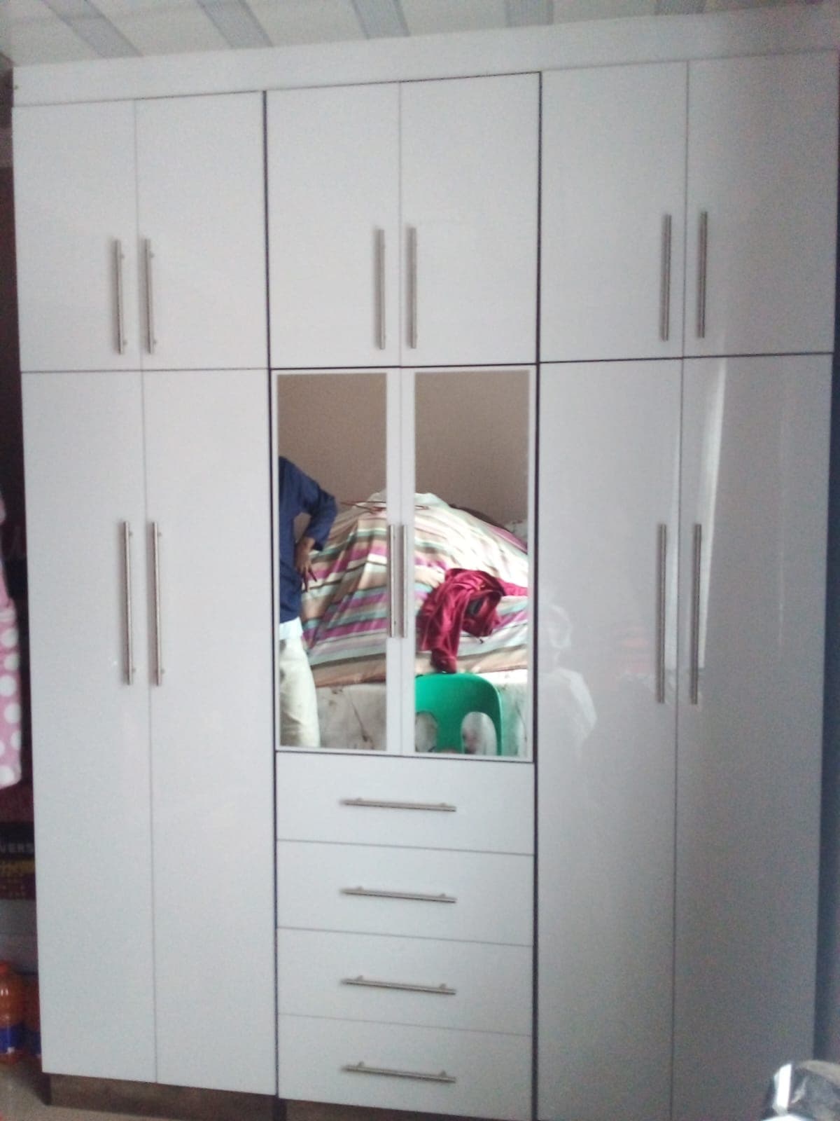Glossy white floor-to-ceiling wardrobe with silver handles, central mirrors, and four stacked drawers below.